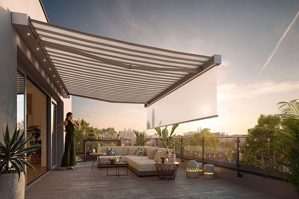 Markise über einer Holzterrasse, im Hintergrund eine Person und Pflanzen sowie ein Sonnenuntergang. Markise über einer Holzterrasse, im Hintergrund eine Person und Pflanzen sowie ein Sonnenuntergang.