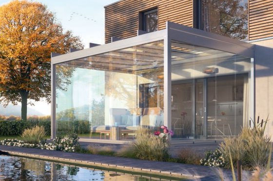 Moderne Überdachung aus Glas und Metall mit Terrassensituation und angrenzendem Wasserbereich, umgeben von Pflanzen.