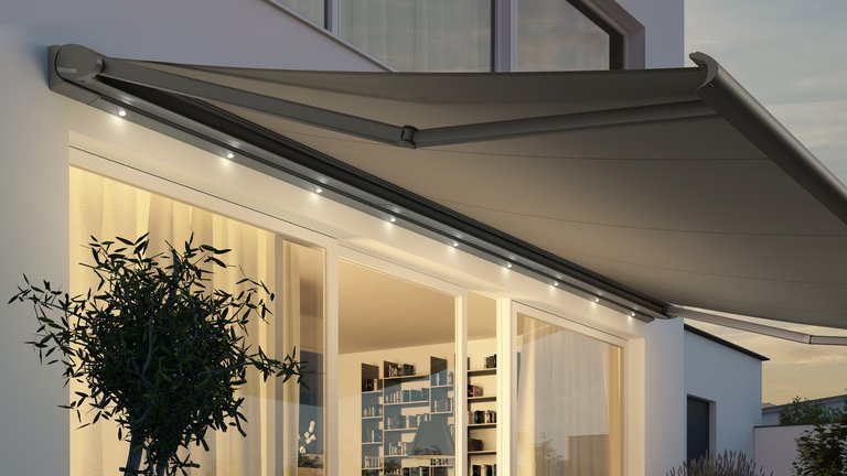 Markise in grauem Design mit LED-Beleuchtung, über einer großen Fensterfläche in einer Terrassensituation.
