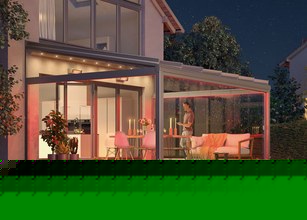 Terrassensituation mit Überdachung, warmem Licht und einer Frau, die den Abend genießt. Grüntöne dominieren. 
