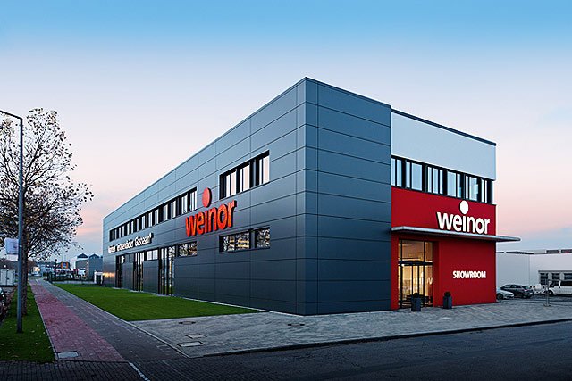 Moderner, rechteckiger Gebäudekomplex in Grau mit roten Akzenten und großen Fenstern.