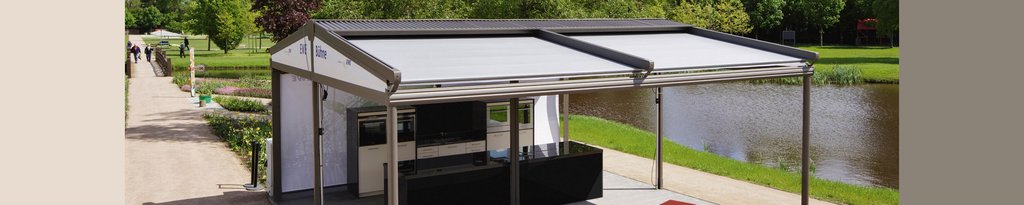 Markise mit Überdachung vor einer Parklandschaft und einem Wasserlauf im Hintergrund.