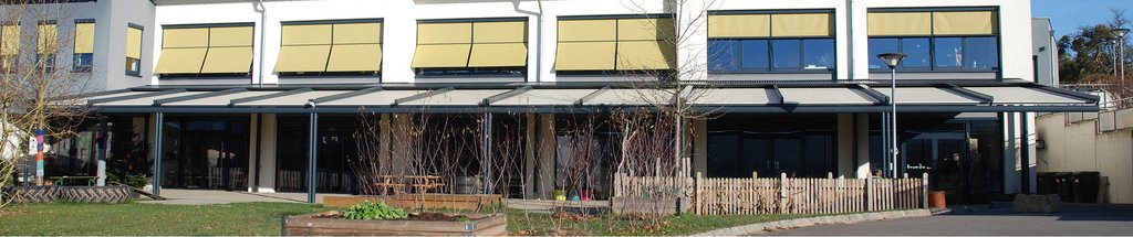 Überdachung vor einem modernen Gebäude mit gelblichen Markisen und großen Fenstern. Überdachung vor einem modernen Gebäude mit gelblichen Markisen und großen Fenstern.